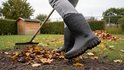 Persoon met grijze broek draagt zwarte Dunlop laarzen tijdens het harken van bladeren.
