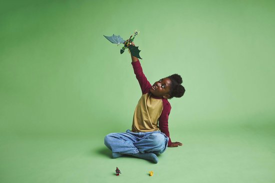 Meisje met afro-kapsel zit en houdt een groene LEGO draak met gespreide vleugels omhoog.