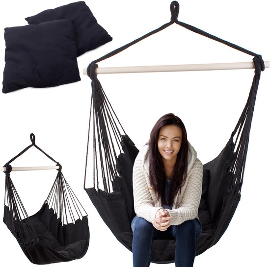 Zwarte hangstoel met een houten spreider, gedragen door touwen. Een vrouw zit in de stoel. Twee zwarte kussens liggen ernaast.