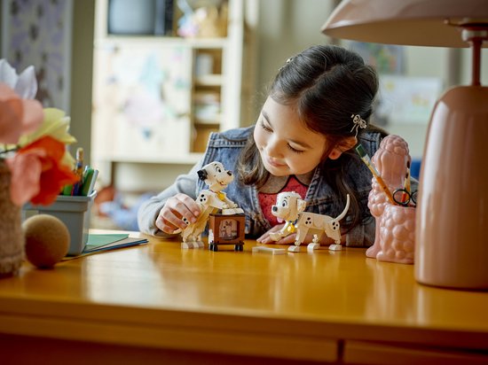 Een meisje bouwt met LEGO Disney Dalmatiërs, waaronder Lucky en Penny bij een televisie.