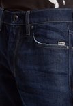 Close-up van een donkerblauwe G-Star jeans met het G-Star Originals label en rafelige rand aan de zak.
