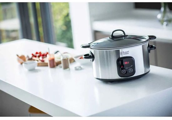 Zilverkleurige Russell Hobbs slowcooker op een aanrecht met ingrediënten op de achtergrond.