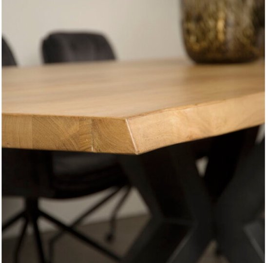 Gros plan du coin d'un plateau de table en acacia naturel sur un piètement noir en X.