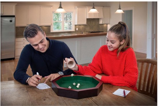 Een man en een vrouw spelen een dobbelspel rond een achthoekige bak met groen vilt. Er liggen zes dobbelstenen in de bak.