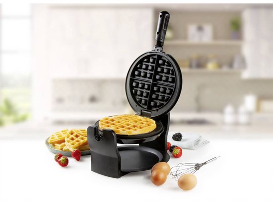 Zwart wafelijzer met een gemaakte wafel, bessentaart, eieren en klopper.