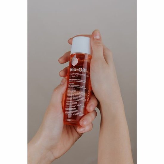 Twee handen houden een flesje Bio-Oil met oranje vloeistof vast.