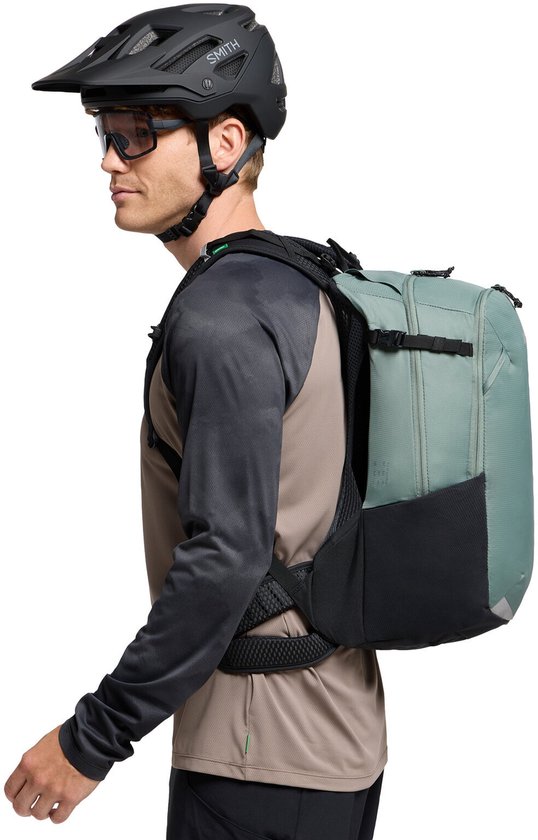 Man in sportkleding met helm en bril draagt een grijze en zwarte rugzak.