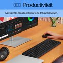 Zwart HP toetsenbord en muis op een bureau met monitor en laptop. Persoon typt op toetsenbord, 12 functietoetsen activeerbaar met één klik.