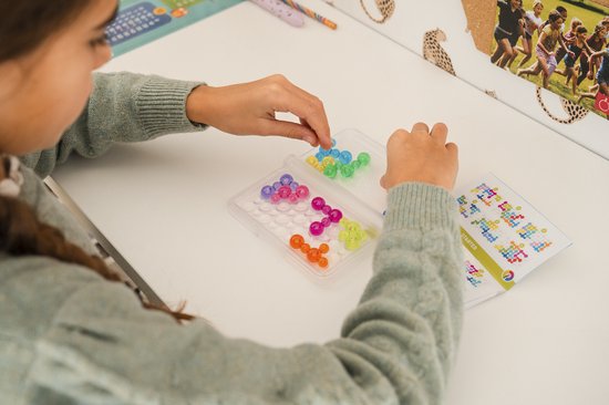 Meisje met vlechtjes plaatst gele en groene spelstukken in een speldoosje met gekleurde bubbels.