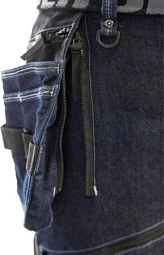 Detail van een donkerblauwe werkspijkerbroek met ritsen en een Blaklader label.