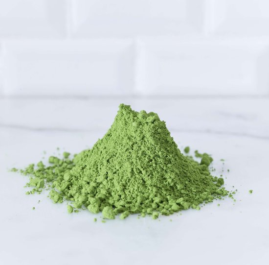 Een hoopje heldergroen matcha poeder op een marmeren ondergrond met witte tegels op de achtergrond.