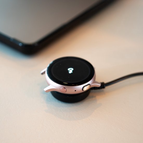 Roze smartwatch met draadloze oplader die naast een telefoon ligt.