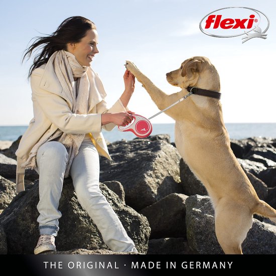 Femme joyeuse tenant une laisse enrouleur Flexi New Comfort rouge, assise sur des rochers au bord de la mer.