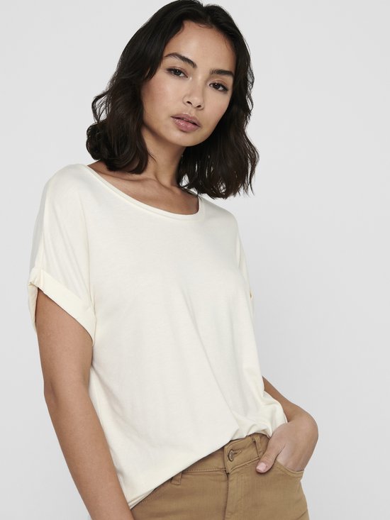 Model in crèmekleurig T-shirt met omgeslagen mouwen en bruine broek.