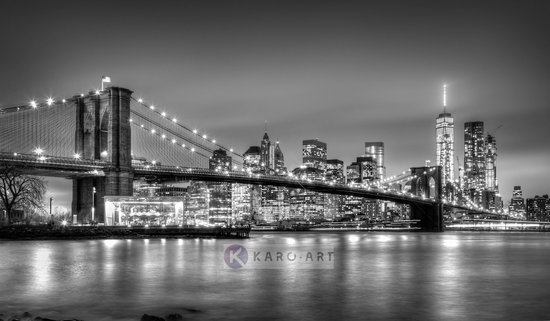 Vue noir et blanc du pont de Brooklyn et de la skyline de New York la nuit, avec les lumières de la ville se reflétant sur l'eau.