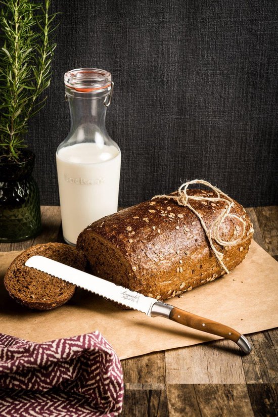 Laguiole Style de Vie broodmes met olijfhouten heft, liggend bij donker volkorenbrood en een fles melk op tafel.
