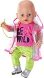 Baby pop draagt roze 'BE WILD' shirt, groene broek, zilveren laarsjes en een doorzichtige regenjas met regenboogprint.