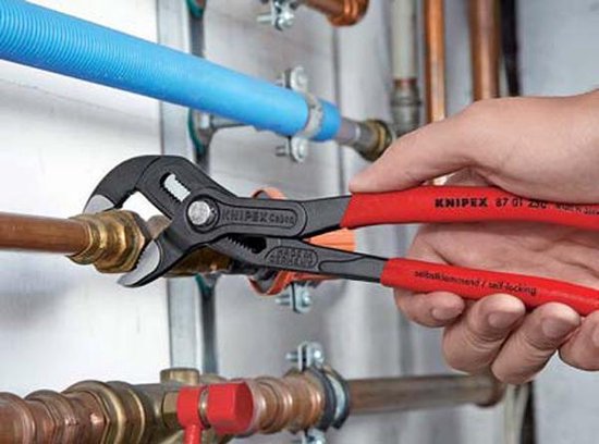 Hand gebruikt een Knipex Cobra waterpomptang op een koperen buis en fitting.