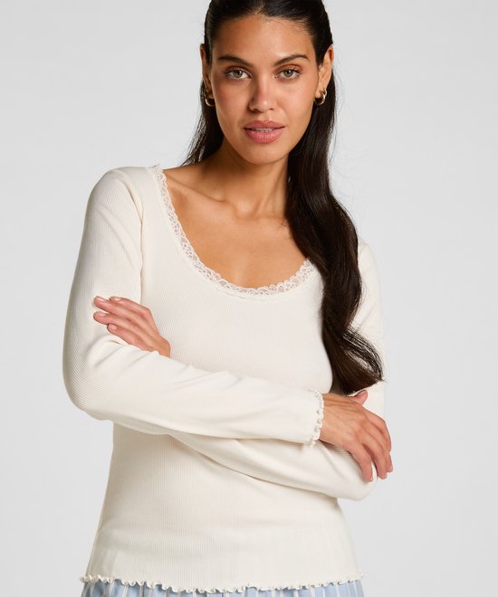 Model draagt een crème-wit ribgebreid shirt met lange mouwen, kanten halslijn en golvende zomen, met de armen gekruist.