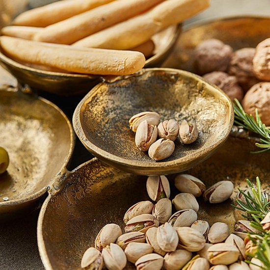 Close-up van een antiekgouden schaalset gevuld met pistachenoten, walnoten en broodstengels.