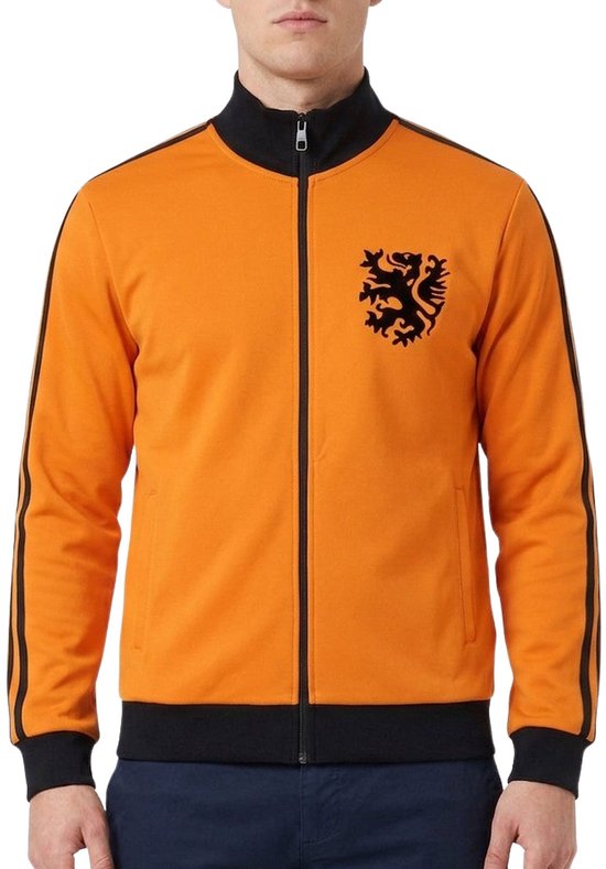 Model draagt een oranje trainingsjack met zwarte details en een leeuwlogo, gecombineerd met een donkerblauwe broek.