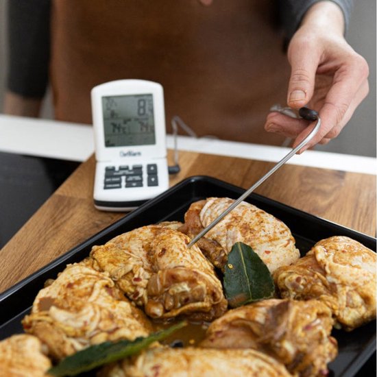 ChefAlarm thermometer op een houten ondergrond, sonde in een ovenschaal met rauwe kip en laurierblaadjes.