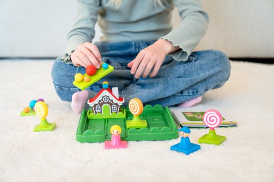 Kind speelt met Hans en Grietje logisch spel met gekleurde ballen, figuren, een huisje en een opdrachtenboekje.