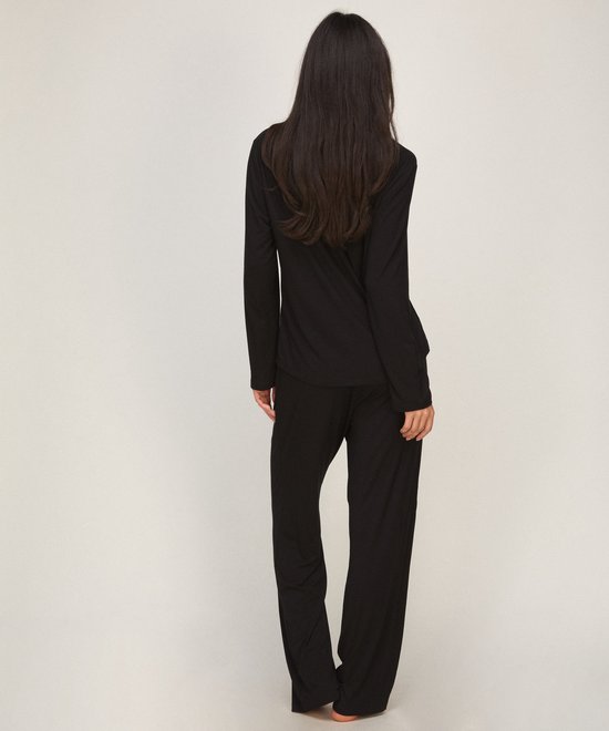 Achteraanzicht van model in een zwarte jersey pyjamaset met lange mouwen en rechte broek.