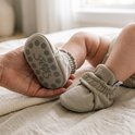 Volwassene houdt een taupe baby-slofje vast met Steppies antislip-zool en elastische enkelband.