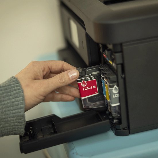 Hand plaatst magenta Brother LC521 M inktcartridge in een zwarte printer.