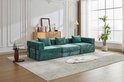 Modulaire bank van donkergroene chenille, met 4 zitkussens en 4 rugkussens, geplaatst op een langwerpig vloerkleed.