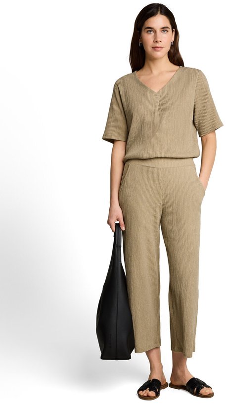 Model draagt een olijfgroene crinkle culottebroek met wijde pijpen, een v-hals top en zwarte tas.