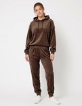 Donkerbruin Apollo velours huispak met capuchon en bijpassende broek, gedragen door een model met witte sneakers.