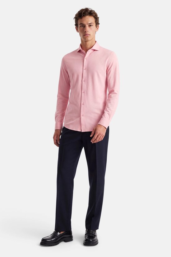 Model in roze piqué overhemd met lange mouwen en donkere broek, staand gepresenteerd.
