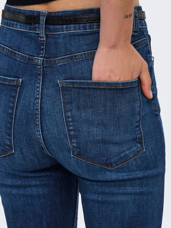 Close-up van de achterzak van een donkerblauwe jeans, met een hand in de zak.