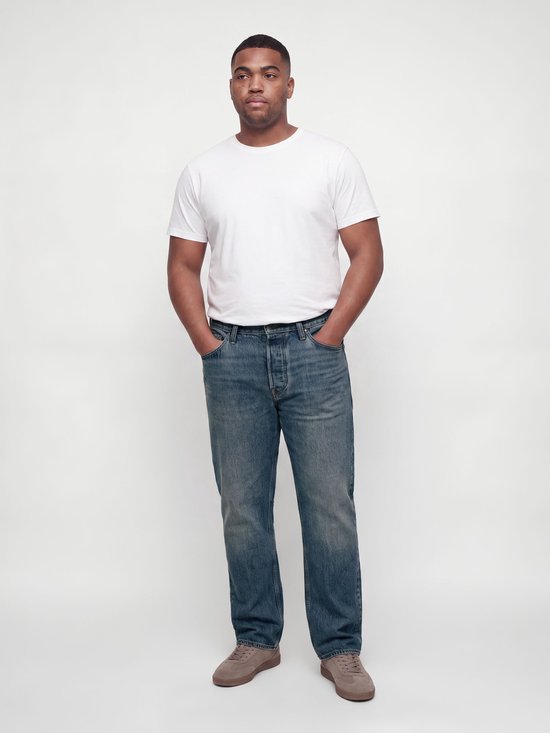 Man met korte mouwen wit T-shirt en blauwe relaxed fit jeans, handen in de zakken.