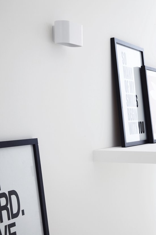 Witte wandlamp met opwaartse lichtstraal, naast ingelijste posters met tekst.