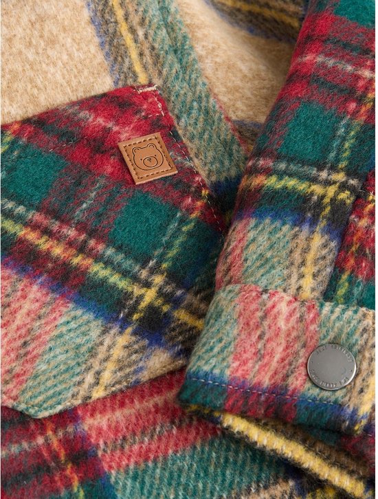 Close-up van beige geruit jack met klein leren label met berenlogo en zilveren drukknop op de mouw.