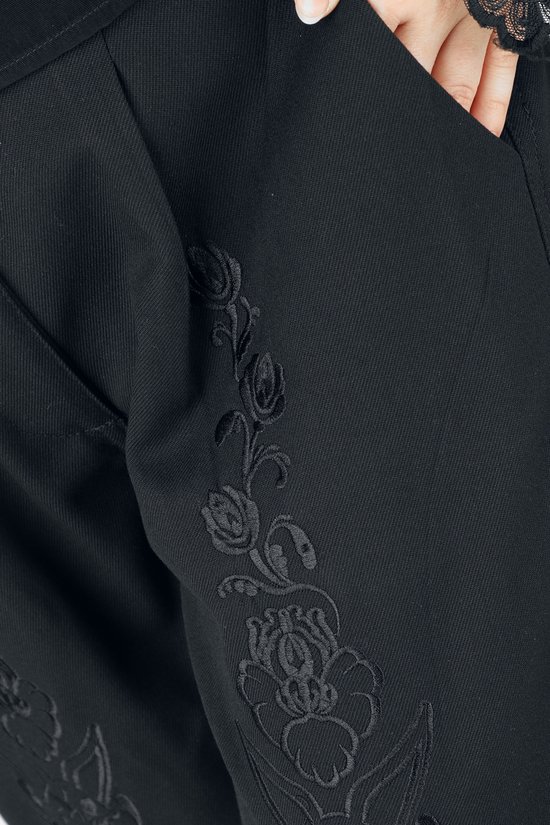 Close-up van een zwarte broek met subtiel, geborduurd bloemenpatroon op het been.