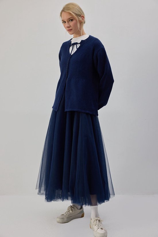 Model draagt een wijde marineblauwe tule rok en een donkerblauw vest over een wit shirt.