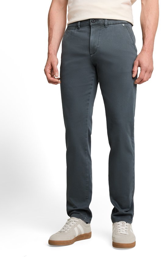 Man in een donkergroene chino broek, beige T-shirt en witte sneakers.