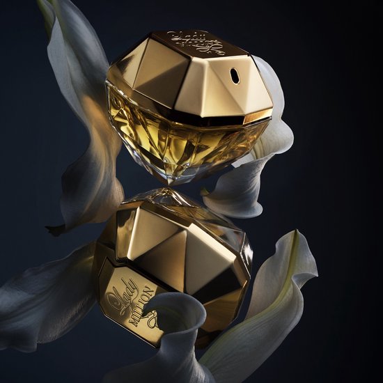 Gouden Lady Million parfumflessen in diamantvorm, omringd door witte bloemen.