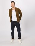 Een man met een witte t-shirt en een olijfgroene bomberjack draagt een donkerblauwe slim fit jeans.