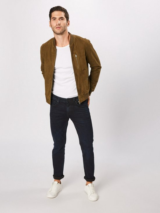 Een man met een witte t-shirt en een olijfgroene bomberjack draagt een donkerblauwe slim fit jeans.