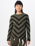 Model met zwarte muts draagt een groene trui met zwarte chevron-strepen.