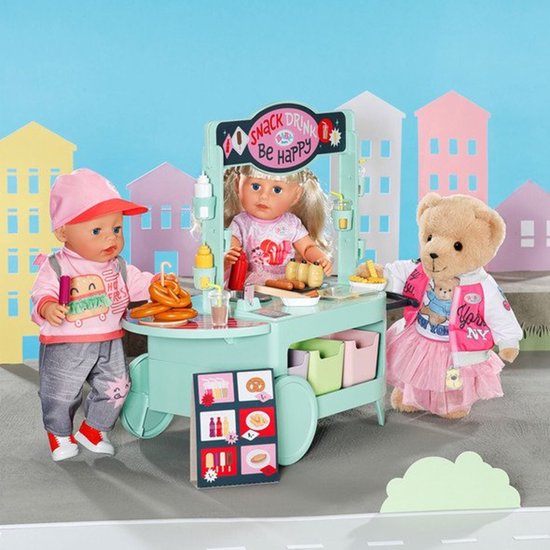 Een BABY born pop en teddybeer bij een mintgroene snackkar met de tekst 'SNACK DRINK Be Happy'.