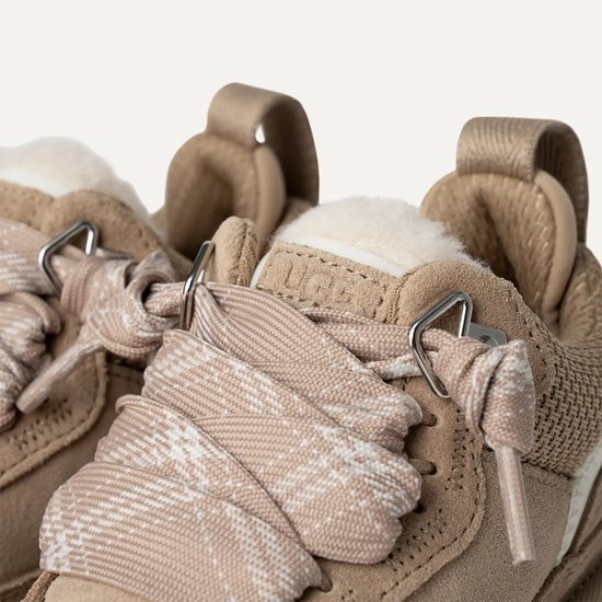 Close-up van beige UGG sneakers met stoffen veters met ruitpatroon en schapenwollen voering.