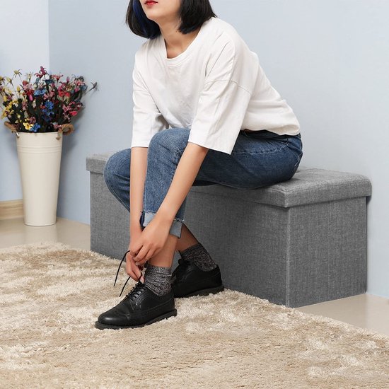 Grijze opbergkist, een vrouw met een witte top en jeans knoopt haar schoenen.