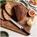 Karthuis broodmes met zwart handvat, snijdt een brood op een houten snijplank. Naast het brood staan plakjes boter en jam.