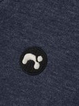 Detailopname van een donkerblauwe trui met een rond zwart label met witte opdruk.